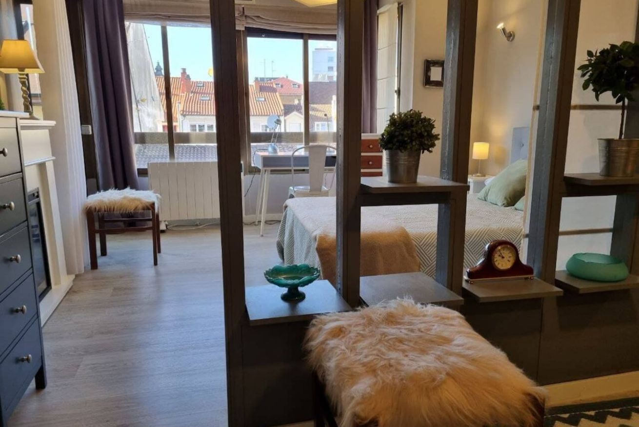 Een hotelkamer met een bed, een stoel, een tafeltje met een kom, een klok en een plant.