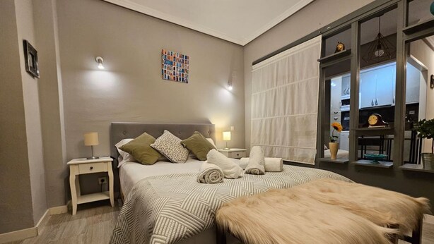 Een slaapkamer met een bed, nachtkastjes, een bont plaid en uitzicht op de keuken.