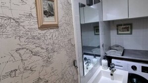 Een badkamer met behang met een wereldkaart, een wastafel, een spiegel en een wasmachine.
