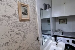 A bathroom with a map wallpaper, a sink, a mirror, and a washing machine.
