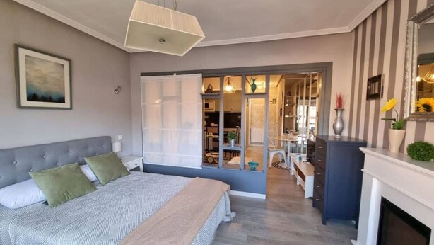 A bedroom with a bed, bedside tables, a dresser, a mirror, and a fireplace.