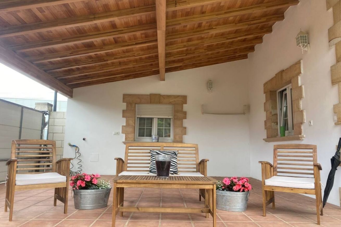 A covered patio area with wooden furniture, a table, and potted plants.