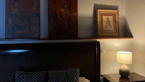 Une chambre avec un lit, une table de chevet avec une lampe et deux œuvres d’art encadrées accrochées au mur.