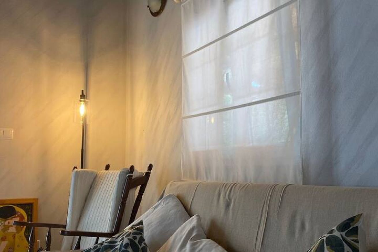 Une pièce comprenant un canapé, un fauteuil, une lampe et une fenêtre ornée de rideaux légers.