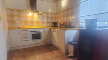 Une cuisine avec un plan de travail recouvert de carreaux, une cuisinière, un lave-vaisselle et une poubelle.