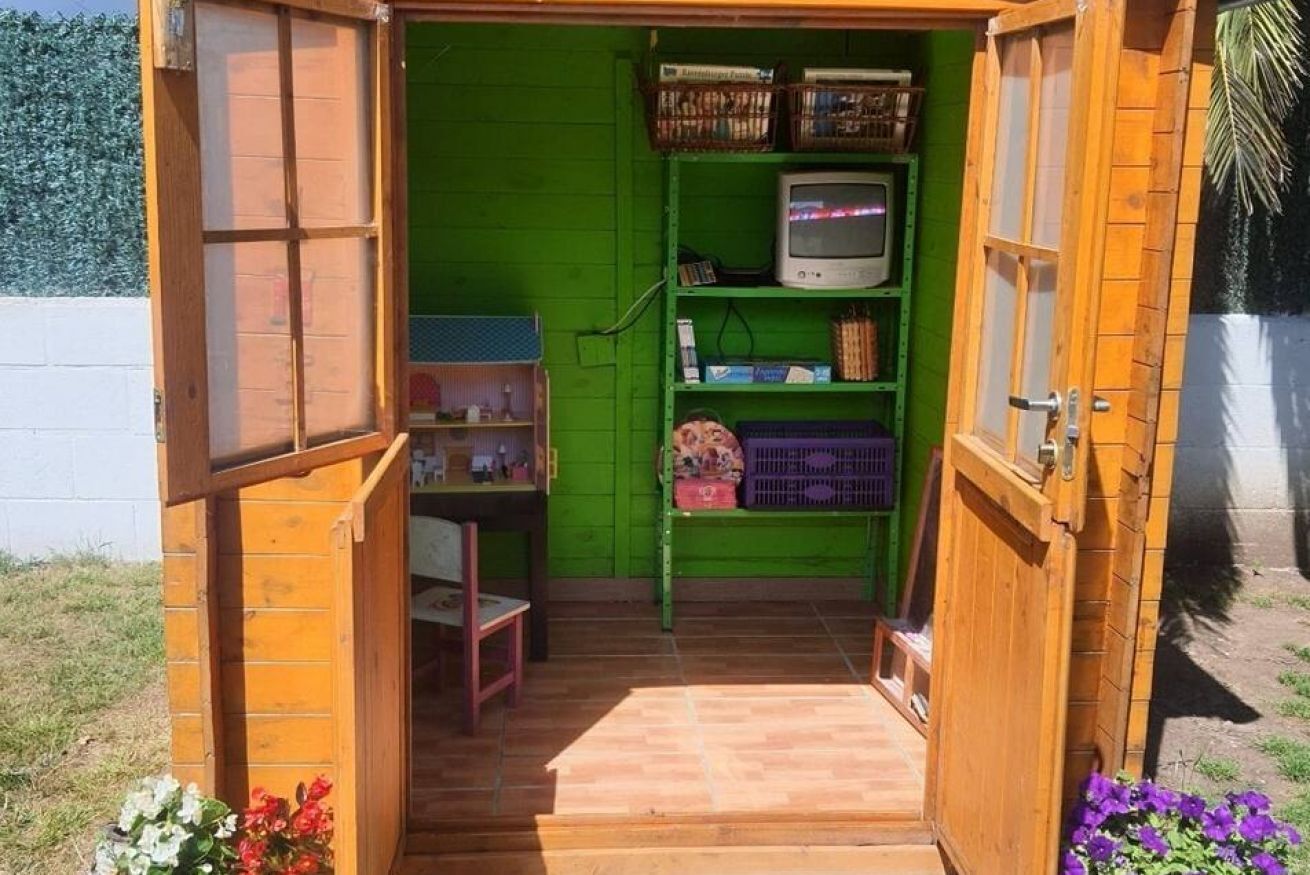 Une petite construction en bois, avec un intérieur vert, un téléviseur posé sur une étagère et une porte donnant sur l’extérieur.