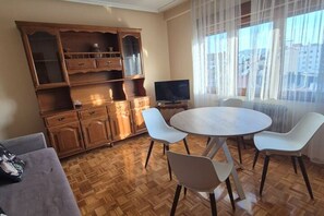 A room with a wooden cabinet, a television, a round table with chairs, and a window with curtains.