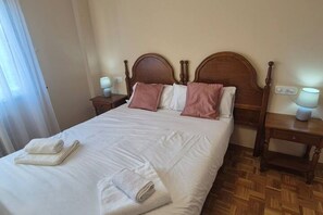 A neatly made bed with white linens and pink pillows, a wooden headboard, and two bedside tables with lamps.