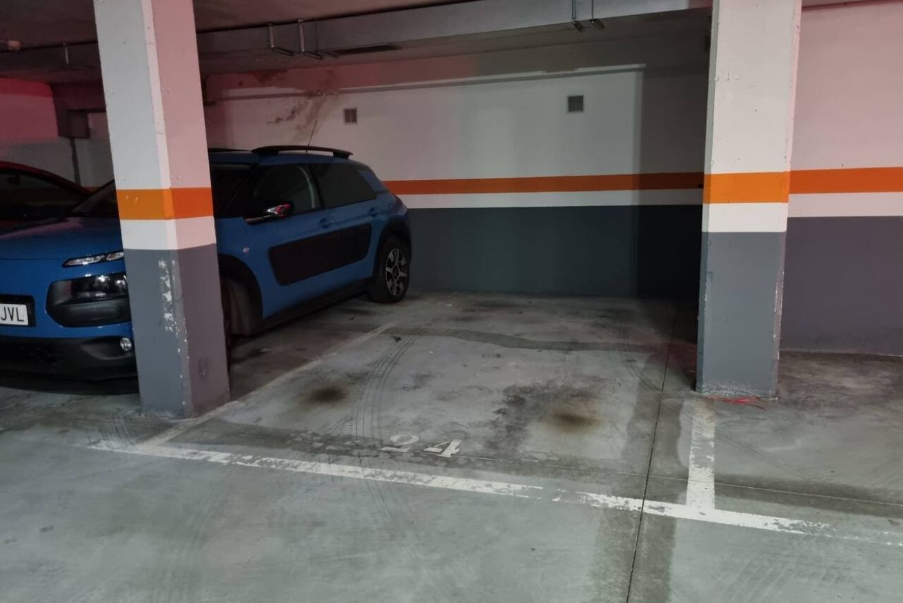 Un estacionamiento con un coche azul estacionado bajo un pilar.