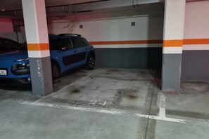 A parking garage with a blue car parked under a pillar.