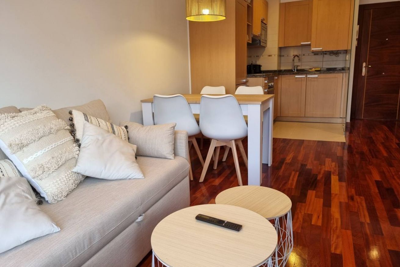 A living room with a sofa, two round tables, a dining area with chairs, and a kitchen in the background.