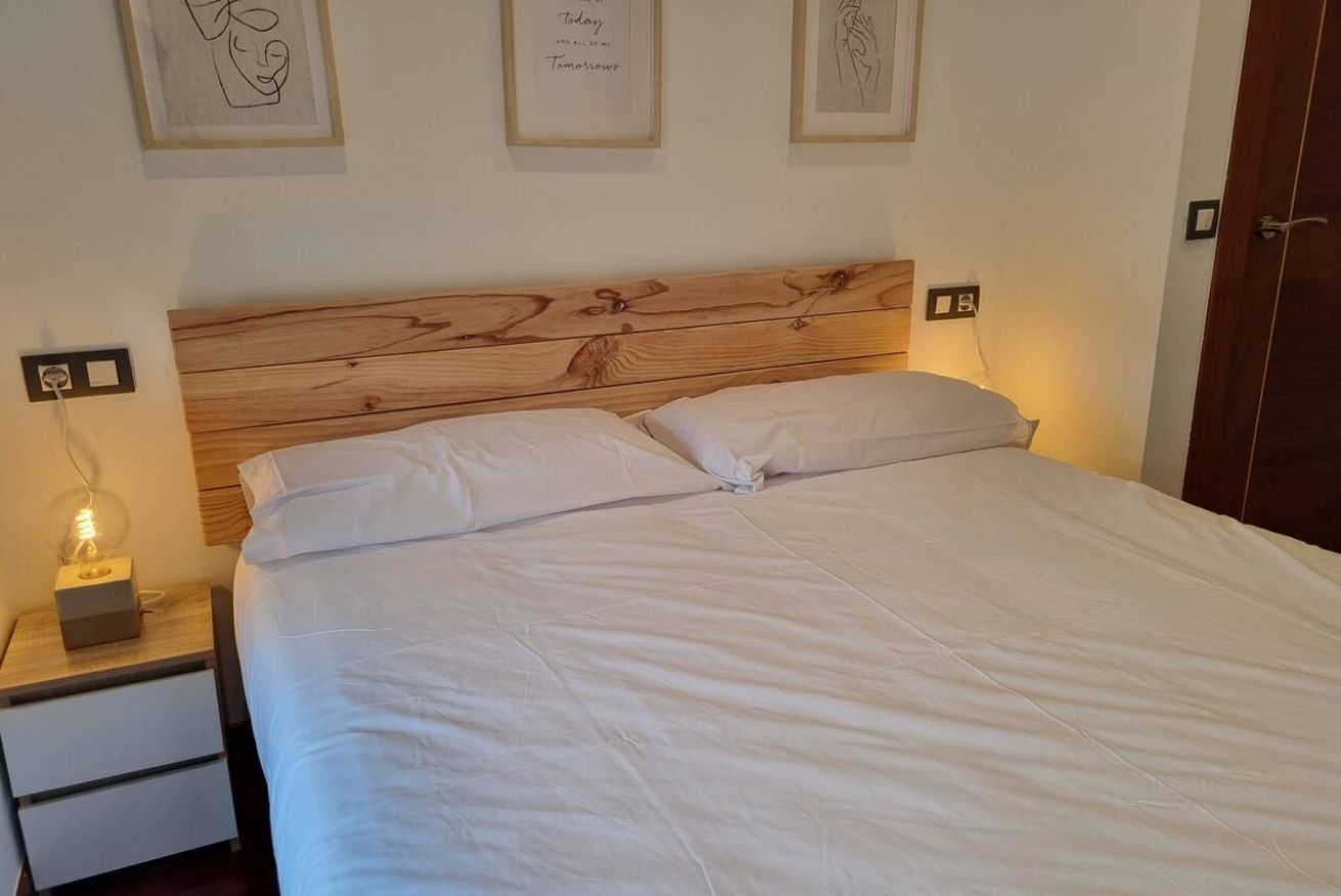 Una cama bien hecha con cabecera de madera, una mesita de noche con lámpara y cuadros en la pared.