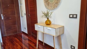 A hallway with wooden flooring, a white console table with a vase, and a round mirror on the wall.