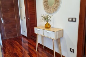 A hallway with wooden flooring, a white console table with a vase, and a round mirror on the wall.