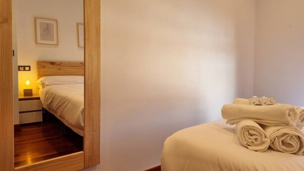 A hotel room with a bed, a nightstand, a mirror, and a wall-mounted picture.