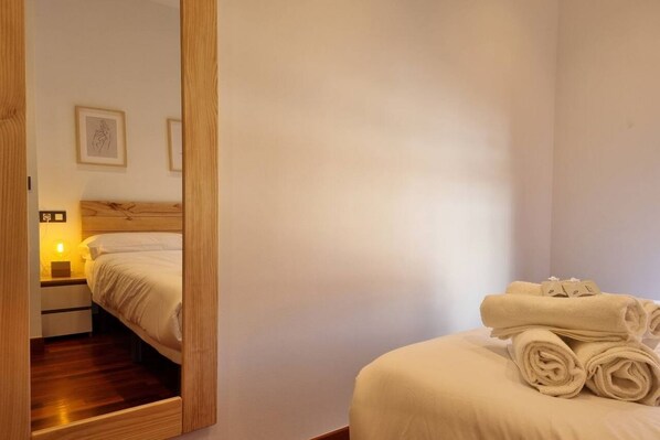 A hotel room with a bed, a nightstand, a mirror, and a wall-mounted picture.