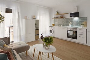 Une cuisine moderne équipée d’un lave-linge, d’un four et d’un four à micro-ondes. On y trouve également un coin repas avec une table blanche et un canapé.