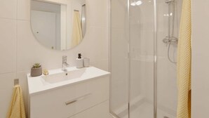 A bathroom with a glass-enclosed shower, a white sink with a mirror above it, and a towel rack with a yellow towel. - 155A Apto Puerto Deportivo by R2R Consulting (Gijón)