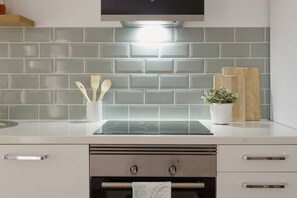 Une cuisine au design moderne, dotée d’une hotte en acier inoxydable, d’un plan de travail blanc et d’un pare-feu gris. On y trouve des ustensiles en bois dans un présentoir et une plante en pot sur le plan de travail.