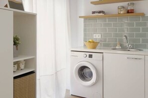 Une cuisine moderne équipée d’un lave-linge intégré, d’un évier et d’une étagère où sont rangés des bocaux.