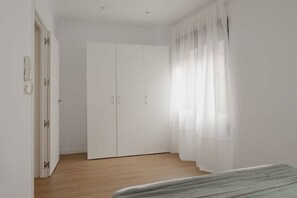 Une chambre à coucher avec une armoire, un lit et une fenêtre ornée de rideaux légers.