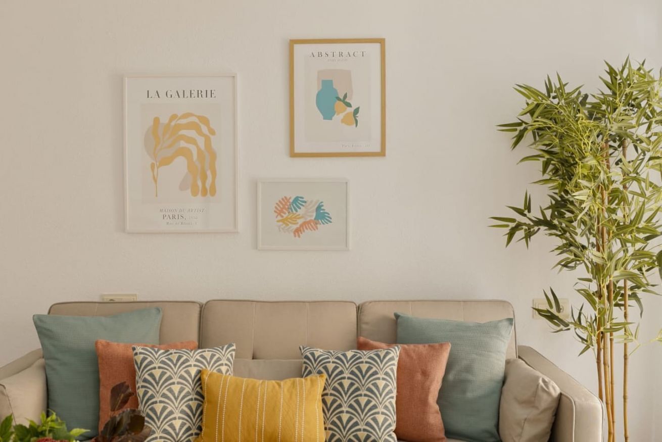 Una sala de estar con un sofá color beige, cojines estampados y tres cuadros enmarcados en la pared.