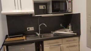 Kompakti keittiö, jossa on mikroaaltouuni, pesuallas ja pieni jääkaappi.
