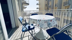 A balcony with a round table and blue chairs, overlooking a residential area with balconies. - Modern Apartment Near the Beach in Jesolo, Italy (Jesolo)