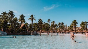 A beach with clear blue water, palm trees, and people swimming and walking on the sand. - Modern Apartment Near the Beach in Jesolo, Italy (Jesolo)