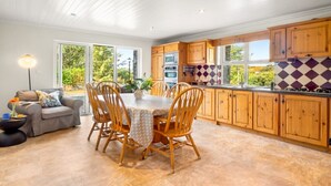 A modern kitchen with wooden cabinets, a dining table with chairs, and a large window providing a view of greenery outside. - Sycamore Cottage on the outskirts of Clifden (Clifden)