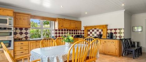 A kitchen with wooden cabinets, a dining table with chairs, a microwave, and a tiled backsplash.