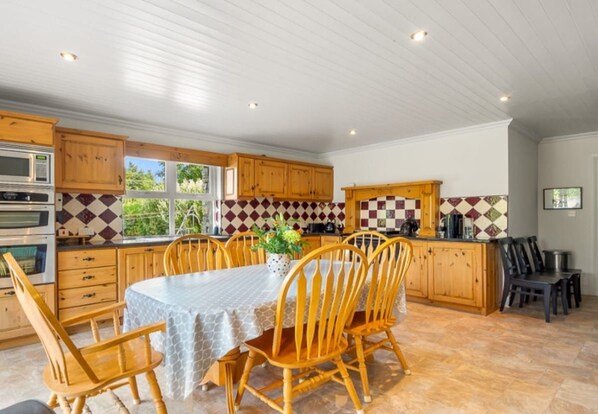 A kitchen with wooden cabinets, a dining table with chairs, a microwave, and a tiled backsplash.