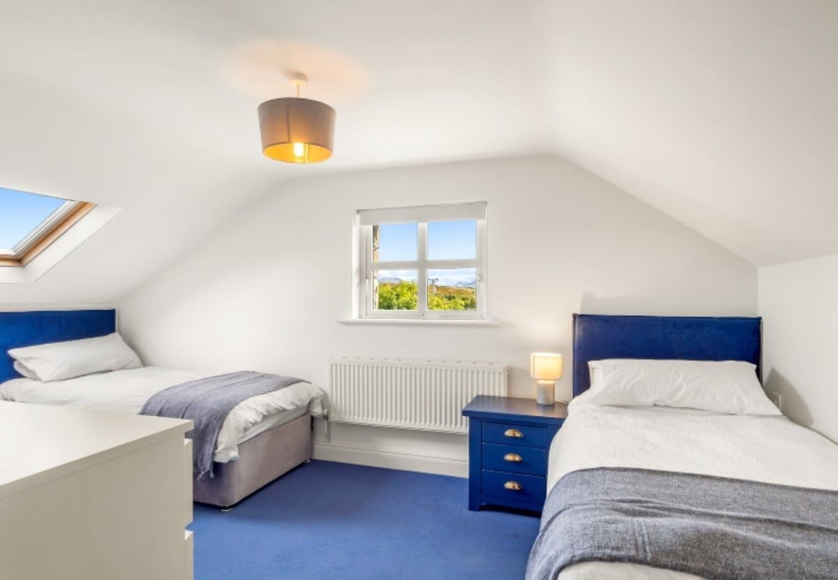 A bedroom with two beds, a window, a radiator, and a ceiling light fixture.