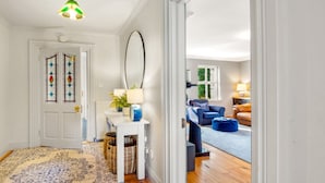 A hallway leading to a living room with a blue sofa, a coffee table, and a lamp. There is a door with stained glass, a white wall, and a ceiling fan. - Sycamore Cottage on the outskirts of Clifden (Clifden)