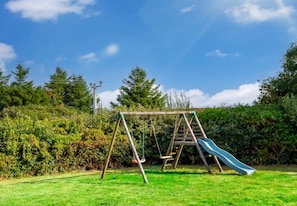 A wooden swing set with a slide in a grassy backyard.