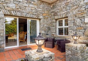 A stone exterior with a patio area, including a wicker chair and a table, and two lantern-style lights.