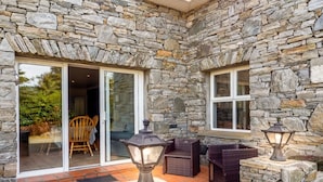 A stone-walled patio with wicker furniture and lanterns, leading to a glass door entrance. - Sycamore Cottage on the outskirts of Clifden (Clifden)