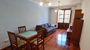 A dining area with a wooden table and chairs, a sofa, and a window with natural light. - 117A Elegant Apartment in Downtown Gijón by R2R (Gijón)