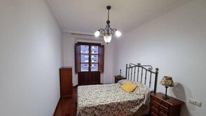 A bedroom with a bed, a wooden dresser, a nightstand, a lamp, and a window with a view of buildings. - 117A Elegant Apartment in Downtown Gijón by R2R (Gijón)