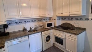 A compact kitchen with white cabinets, a microwave, a washing machine, and a sink. - 117A Elegant Apartment in Downtown Gijón by R2R (Gijón)