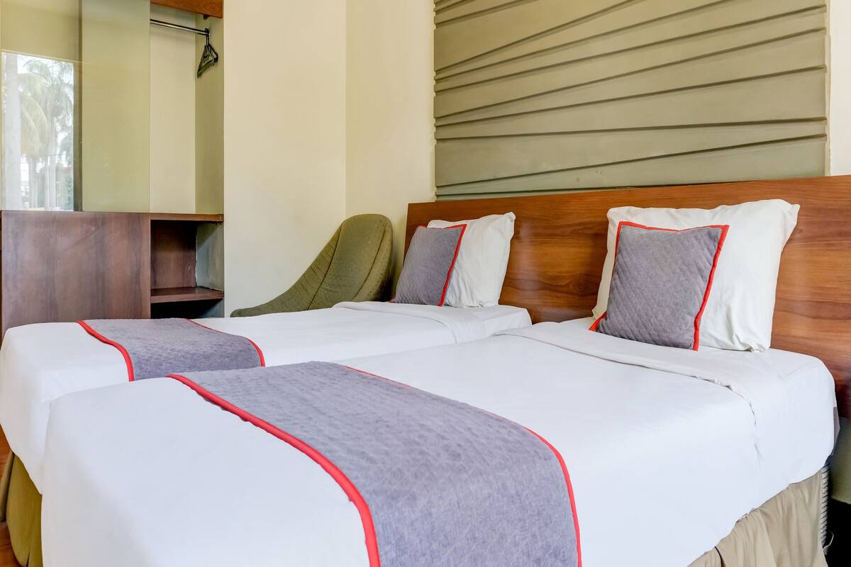 A hotel room with two beds, a wooden headboard, and a seating area with a chair.