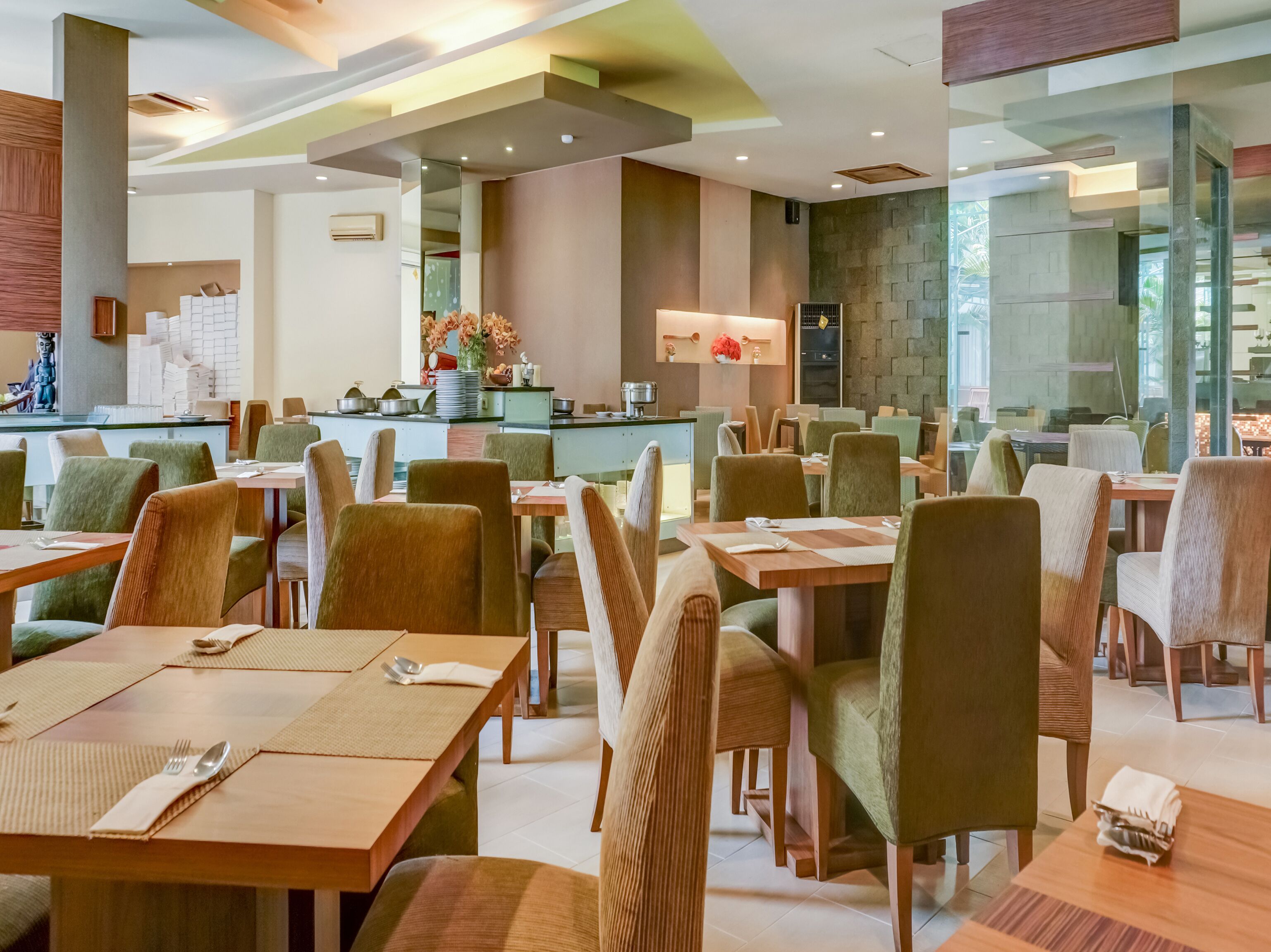 A modern restaurant with multiple dining tables and chairs, a central bar area, and a stone wall.