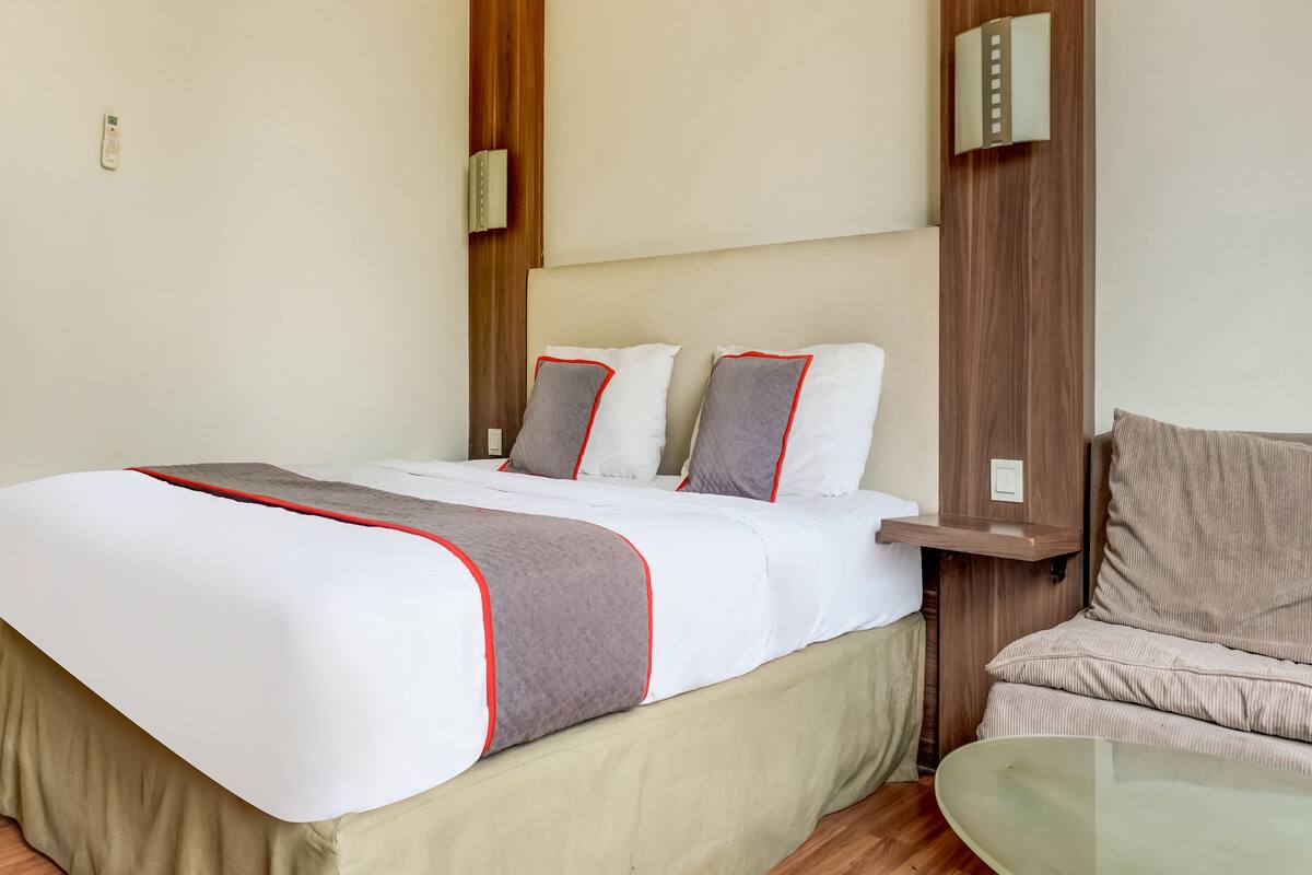 A hotel room with a bed, bedside table, and a chair.
