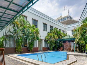 Une piscine dotée d’un toit en verre, entourée de palmiers et bordée d’un bâtiment blanc aux nombreuses fenêtres.