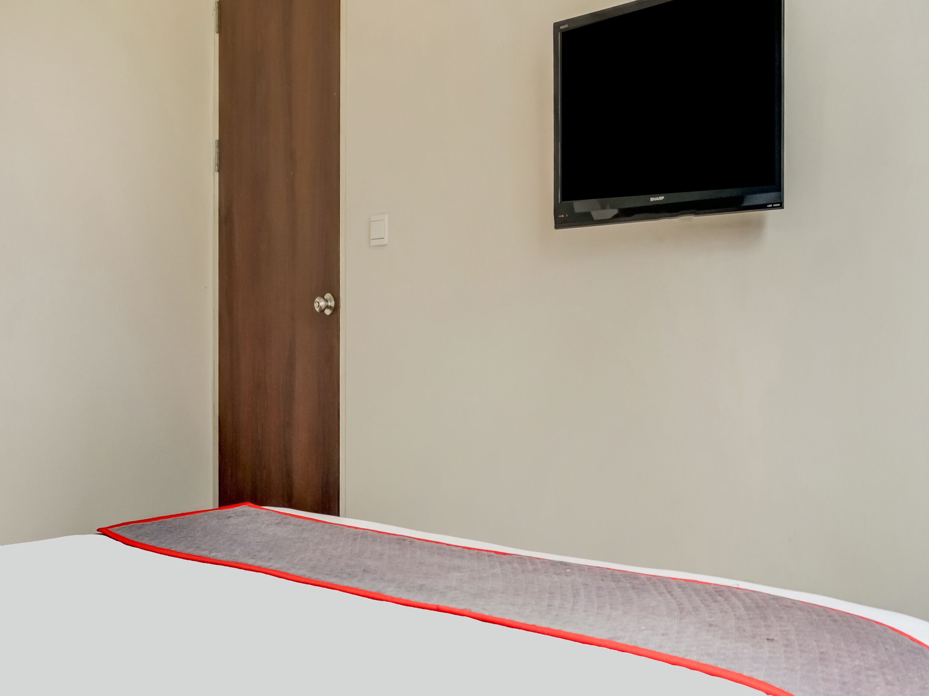 A room with a bed, a wooden door, and a mounted TV on the wall.