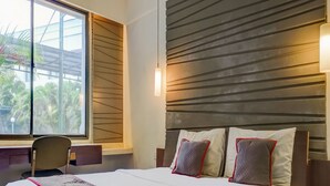 A hotel room with a large bed, a desk, and a window with a view of palm trees. - Townhouse OAK Hotel Grand Cikarang (Cikarang)