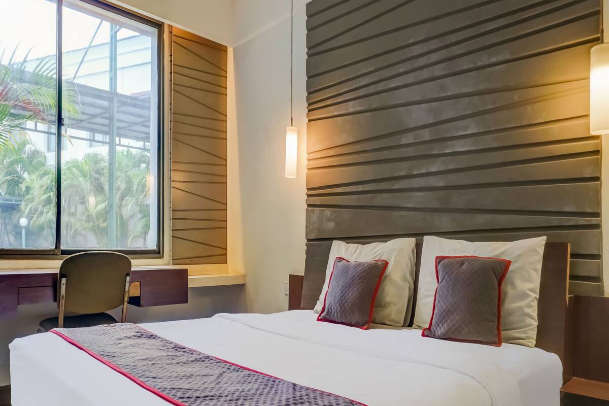 A hotel room with a large bed, a desk, and a window with a view of palm trees.