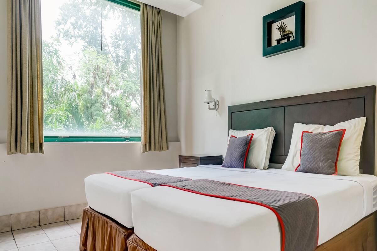 A hotel room with a bed, curtains, a window, a wall-mounted light, and a framed picture.