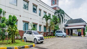 A building with a clock tower, parked cars, and palm trees. - Townhouse OAK Hotel Grand Cikarang (Cikarang)