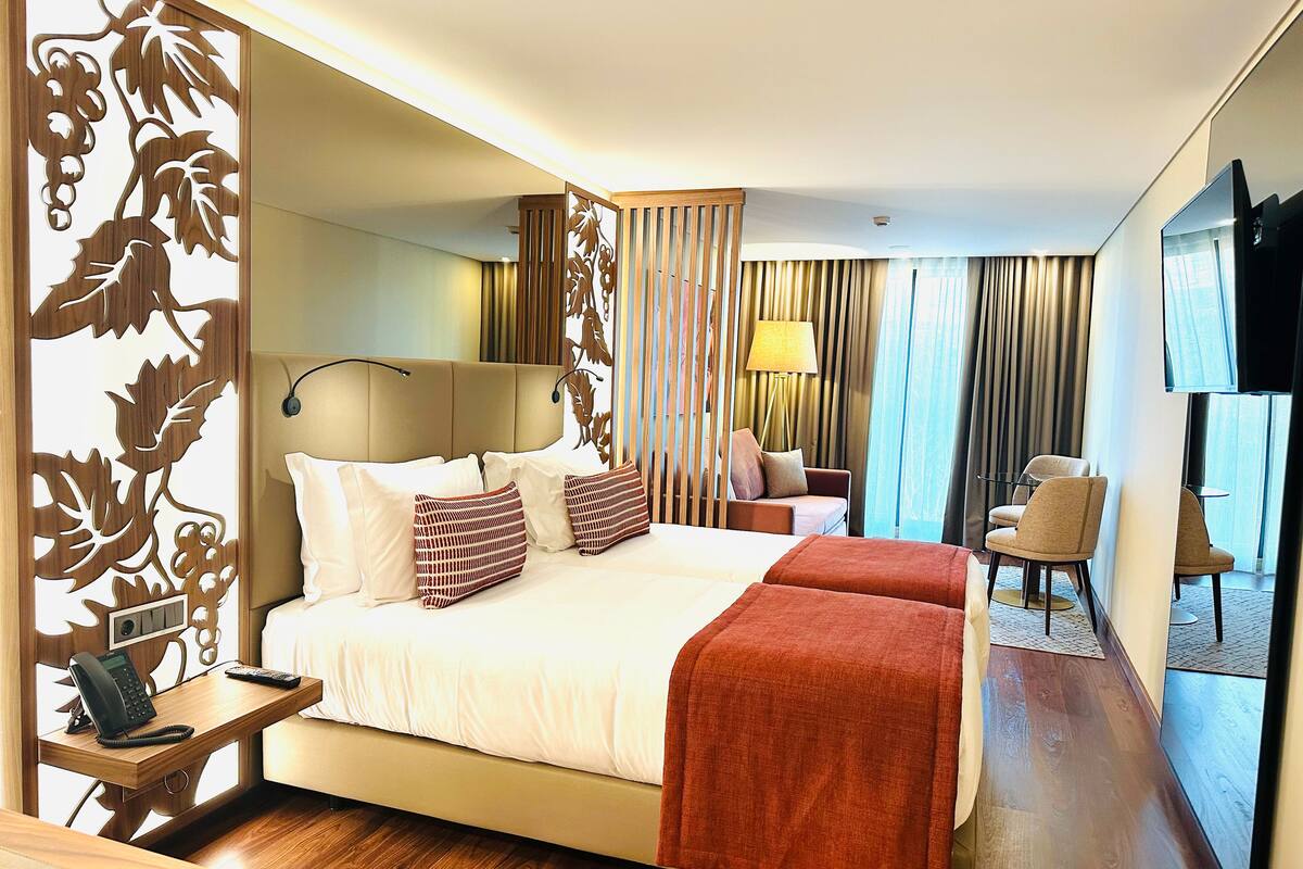 Habitación de hotel con cama, mesita de noche con teléfono, escritorio, silla, televisor y vistas al exterior.